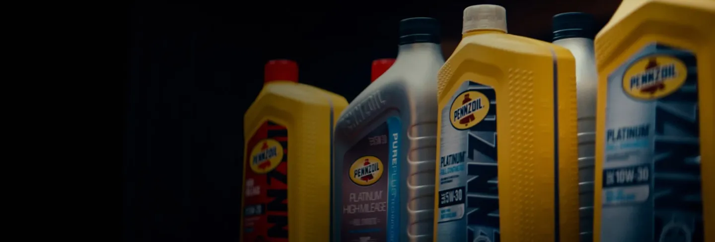 Various Pennzoil motor oil containers in yellow, red, and silver colors arranged in a row against a dark background.
